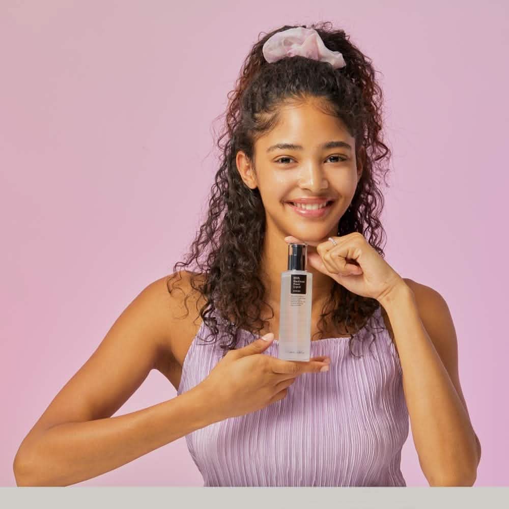 Mujer sosteniendo el CosRx BHA Blackhead Power Liquid. La fórmula de 10 ingredientes con Betaine Salicylate 4% y Niacinamide 2% exfolia poros y reduce marcas post-acné con uso 1–2 veces por semana.