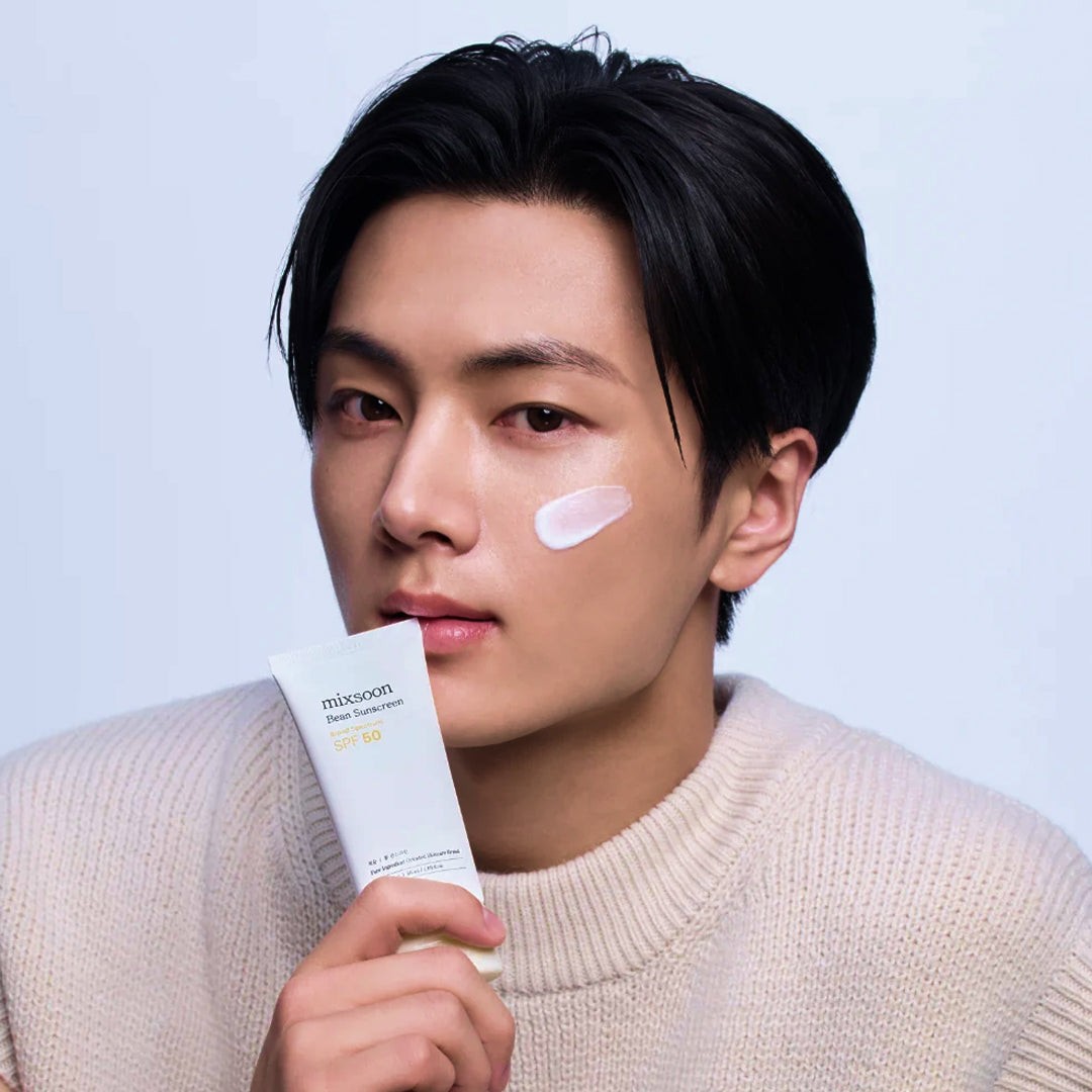 Modelo sostiene el tubo de Mixsoon Bean Sun Serum con una muestra del protector en la mejilla.
