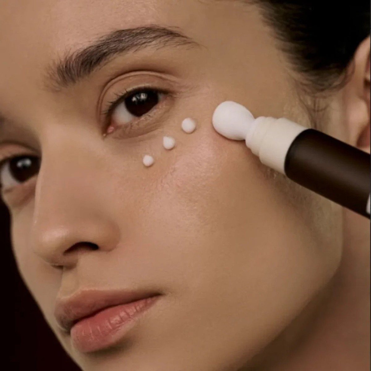 Modelo aplicando SKIN1004 Probio-Cica Bakuchiol Eye Cream con la punta del tubo en el contorno de ojos.