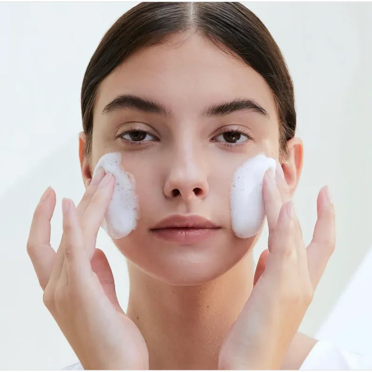 Modelo con espuma de SKIN1004 Tone Brightening Cleansing Gel Foam en las mejillas.