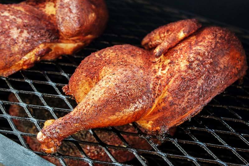 Medios pollos ahumados a leña sobre la parrilla de un ahumador