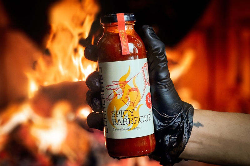 Botella de salsa barbecue artesanal picante frente a las llamas de un ahumador