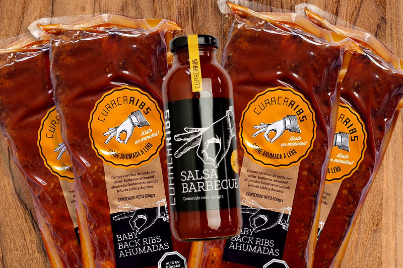 Cuatro costillares barbecue ahumados junto a una botella de salsa barbecue artesanal