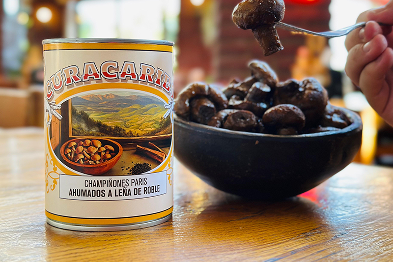 Lata de champiñones ahumados junto a un plato de champiñones servido.