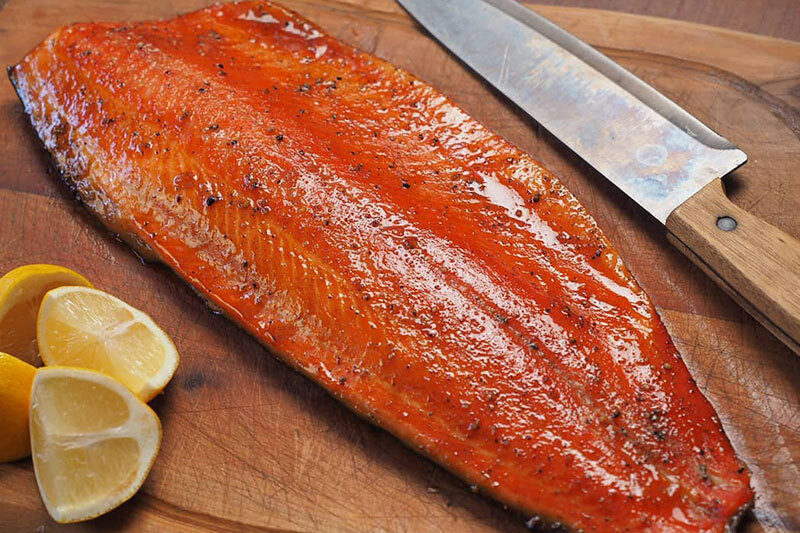 Trucha ahumada laqueada con miel de maple sobre una tabla junto a un cuchillo